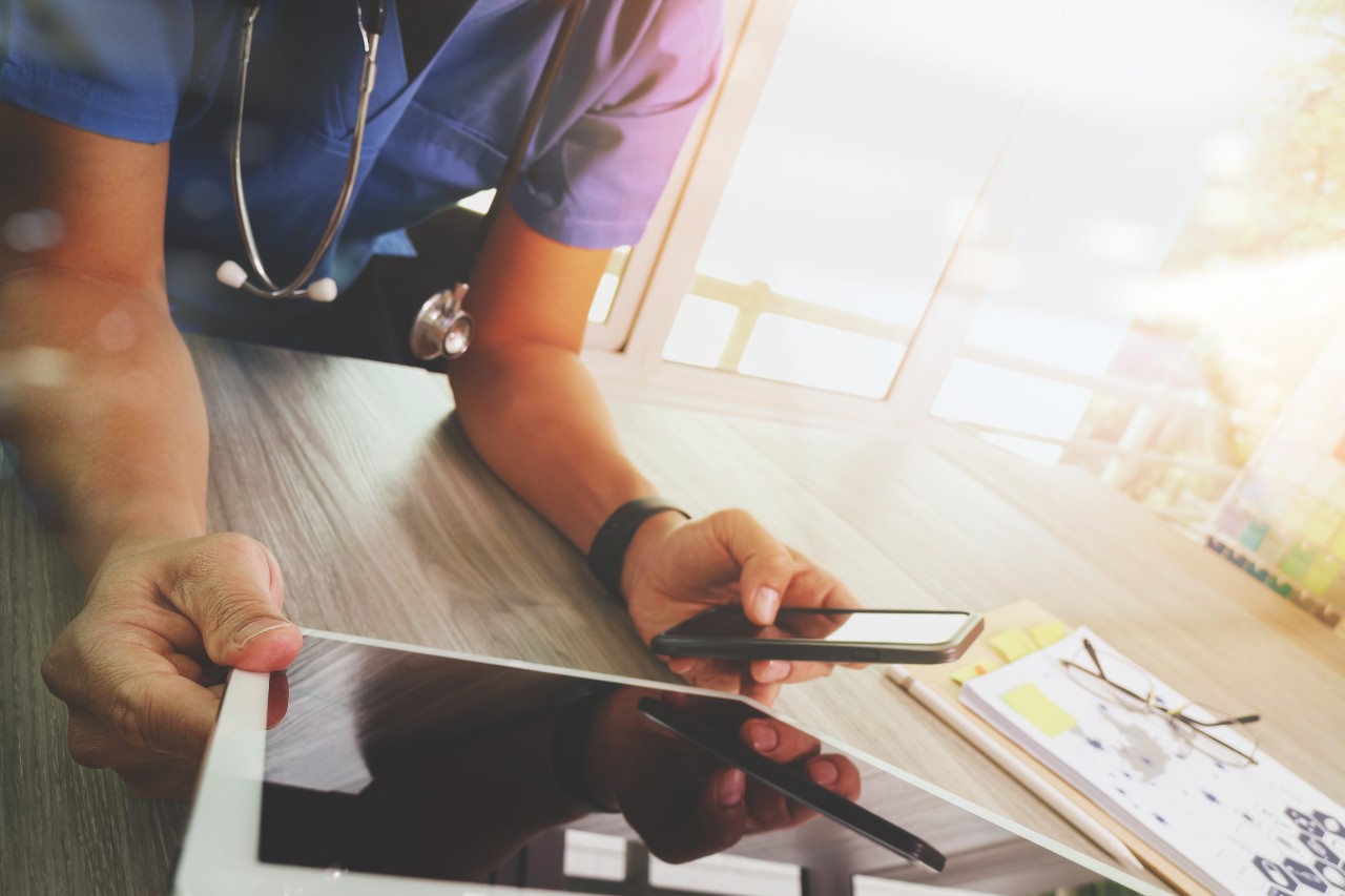 Doctor looking at a phone and tablet while wearing scrubs and a stethoscope