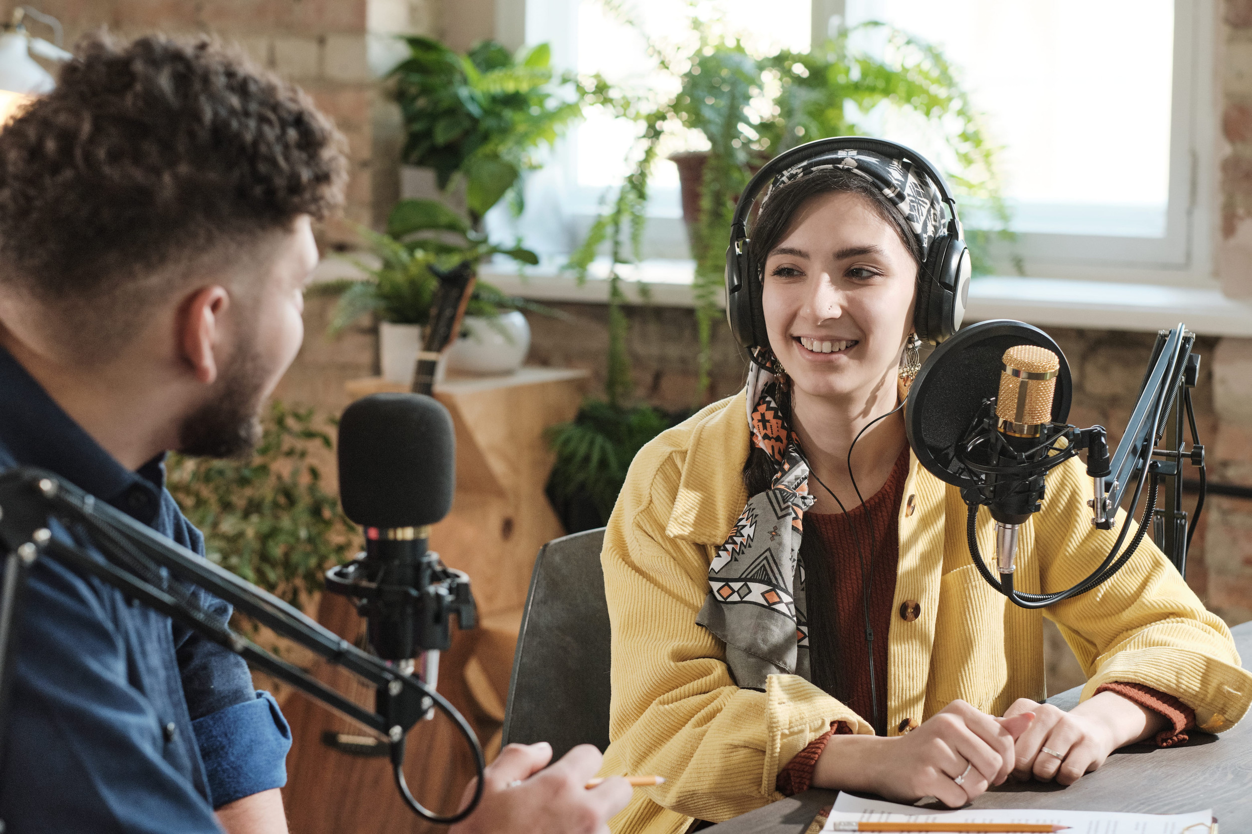 Two hosts wearing headphones talking into microphones in a podcast studio
